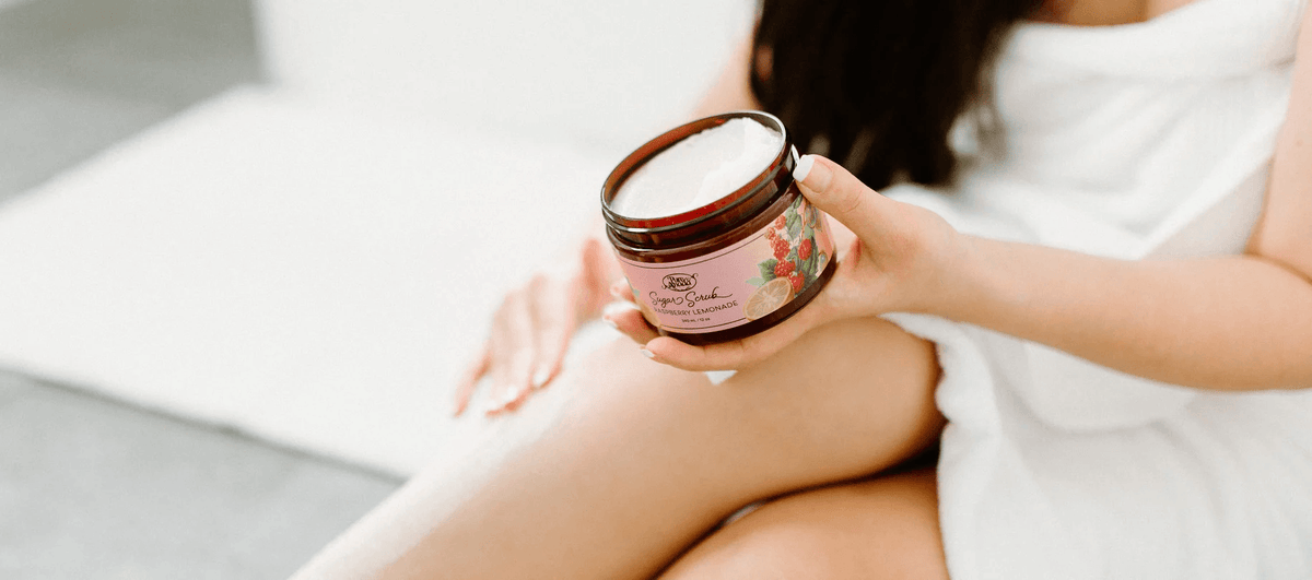 Woman holding a jar of natural body scrubs for exfoliation with raspberry lemonade scent.