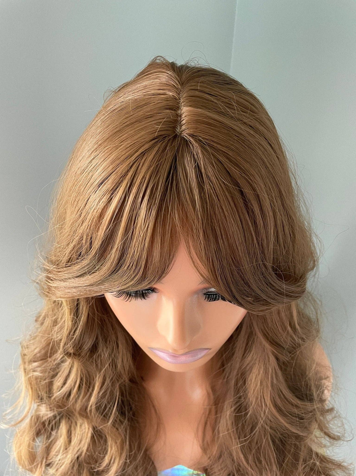 Andrea long brown curly wig with fringe displayed, featuring soft curls and modern curtain bangs.