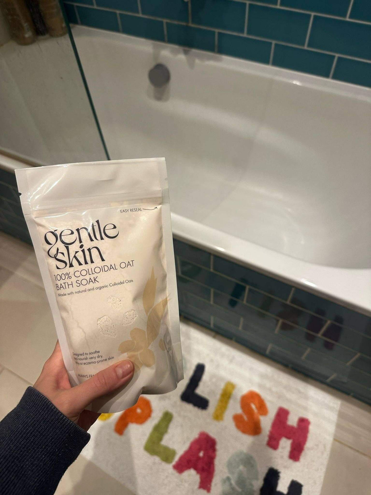 Person holding 100% Organic Colloidal Oat Bath Soak by Gentle Skin in front of a bathtub.