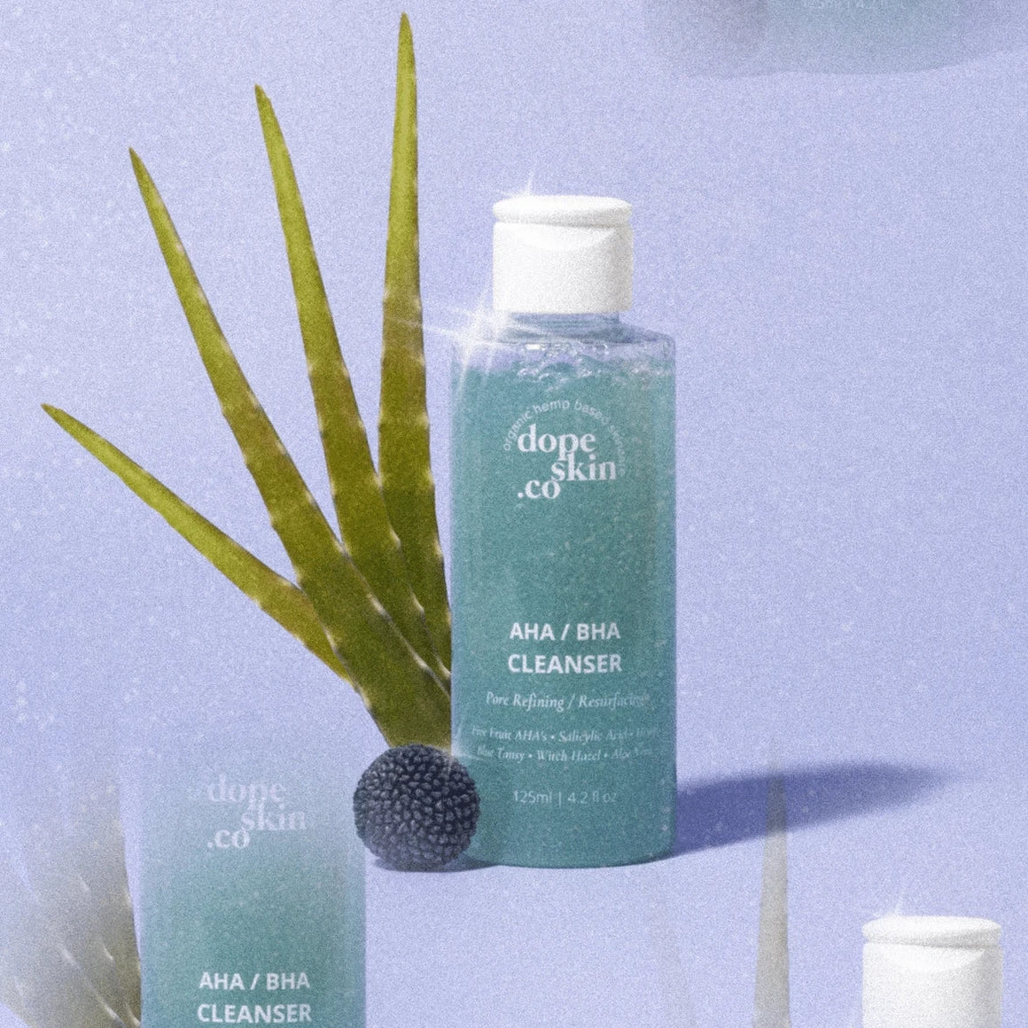 Bottle of 'dope skin co' AHA/BHA Cleanser with aloe vera leaves on a light blue background