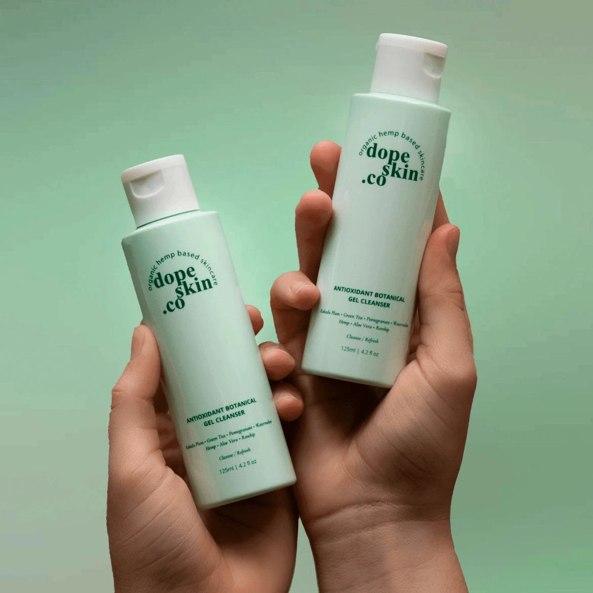 Two bottles of 'dope skin co.' gel cleanser held in hands against a green background