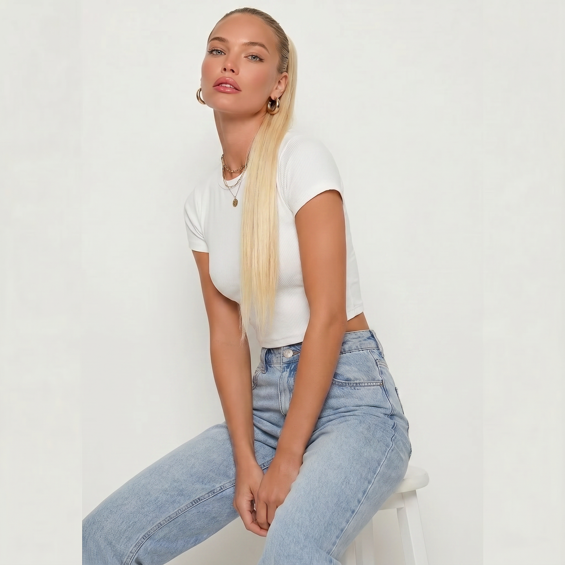 Model showcasing a platinum blonde ponytail hair extension with a stylish white crop top and light blue jeans.