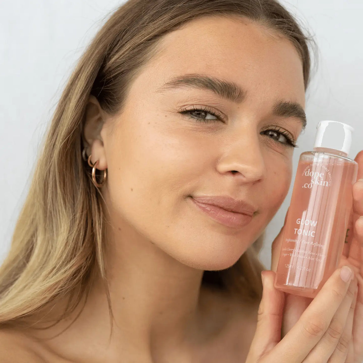 Woman holding Glow Tonic by Dope Skin, showcasing a radiant complexion and glowing skin.