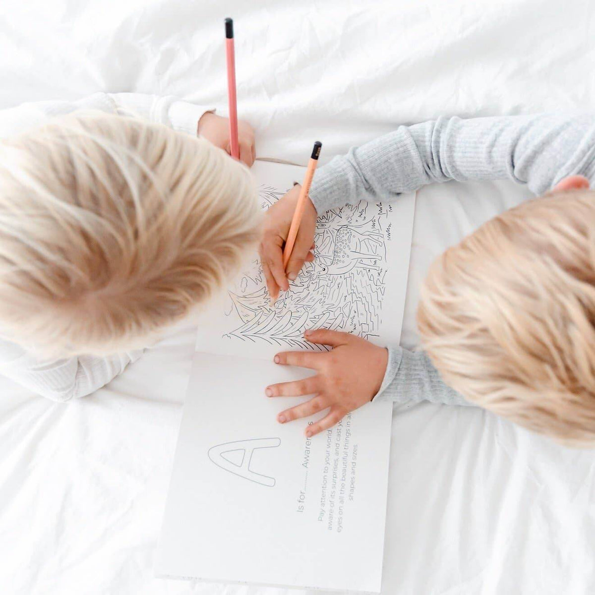Two children coloring on a large sheet of paper with coloring books.