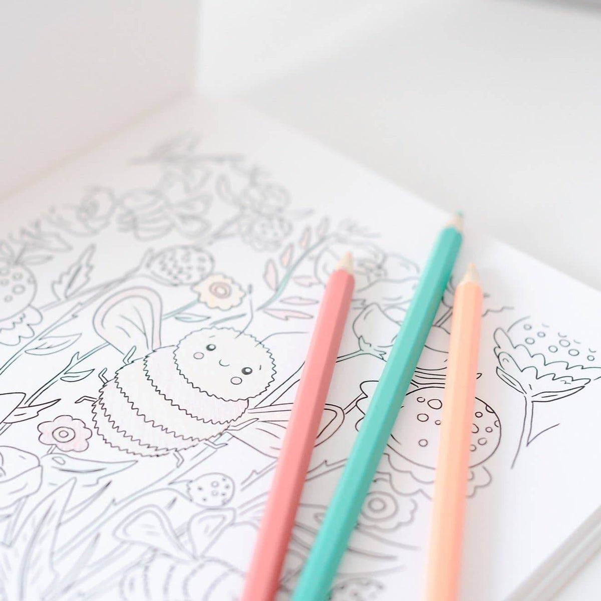 Coloring book with a hedgehog design and three colored pencils on a white surface.