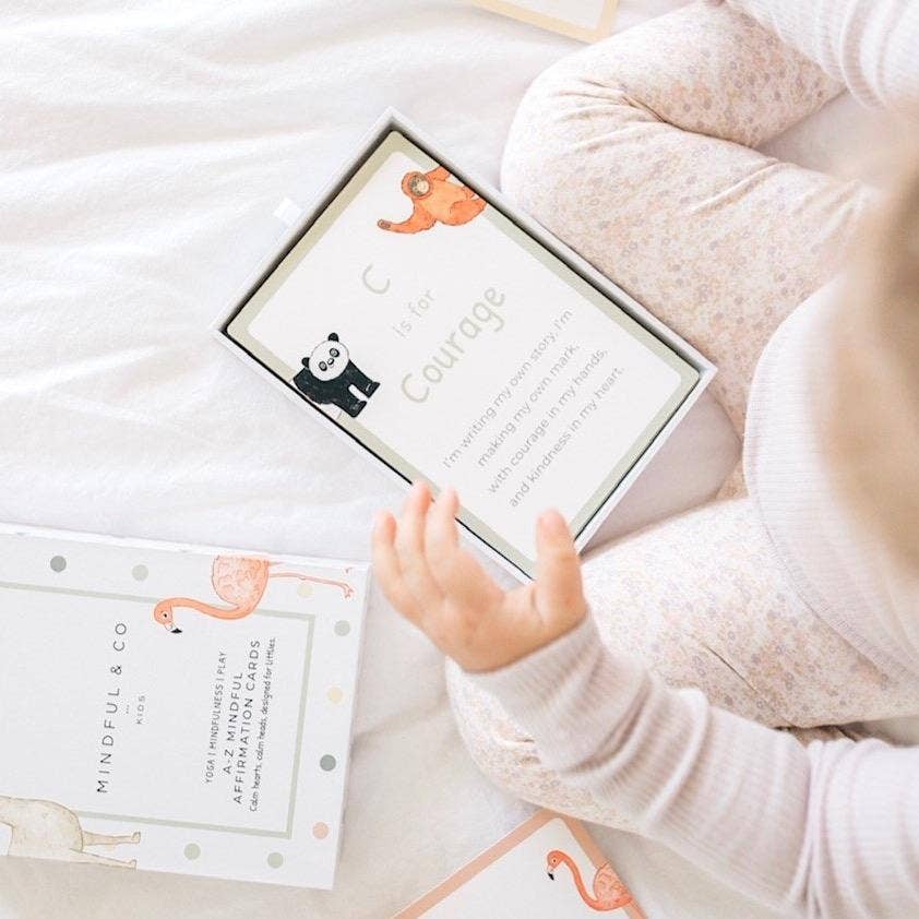 Child's hand reaching towards a box with 'The Courage' card on a soft surface