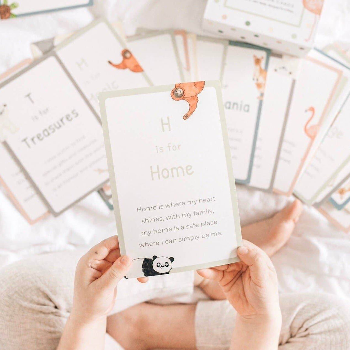 Person holding a card with text and a panda illustration, surrounded by more cards on a soft surface.
