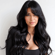 Woman with long, wavy black hair wearing a black top against a neutral background