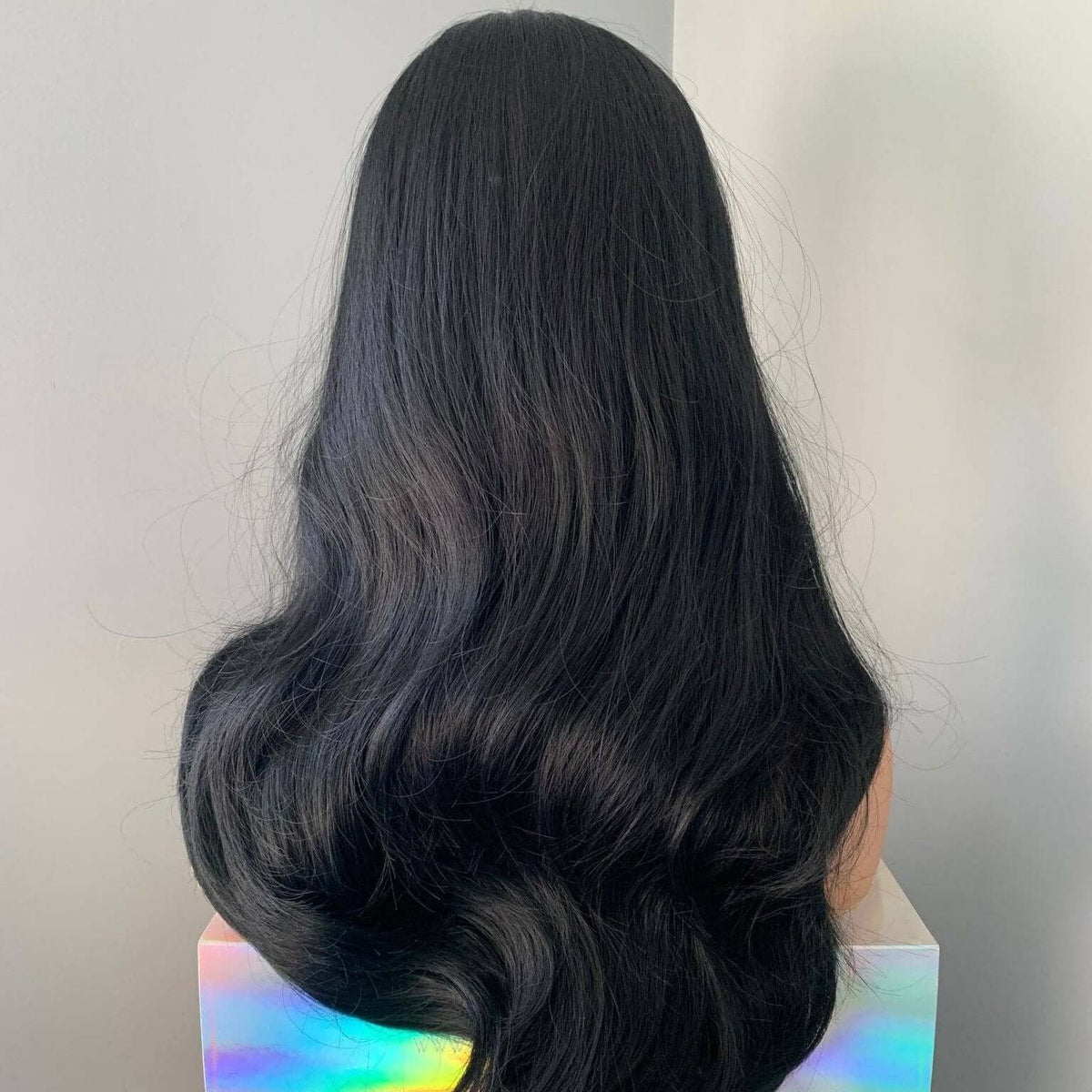 Black wavy hair on a mannequin head with a gray background