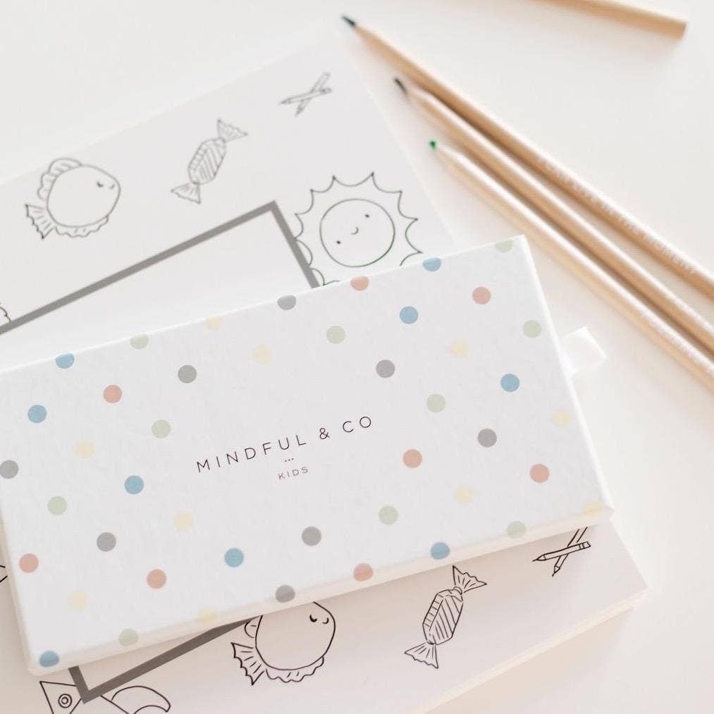 Affirmation Colouring Pencils set packaging with playful dots, lying on coloring sheets designed for kids.