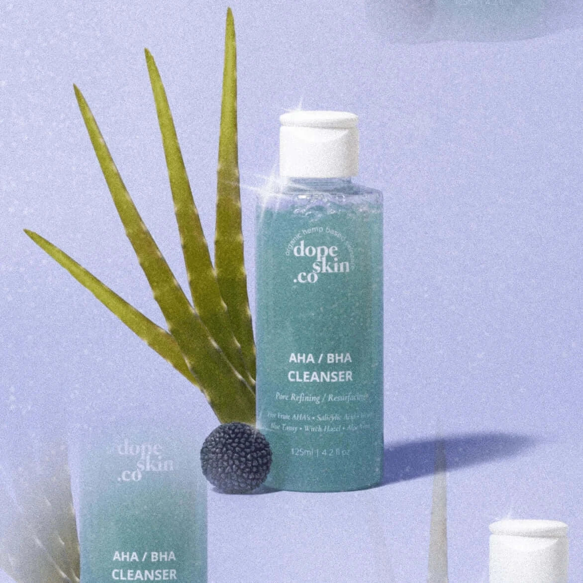 Bottle of 'dope skin co' AHA/BHA Cleanser with aloe vera leaves on a light blue background