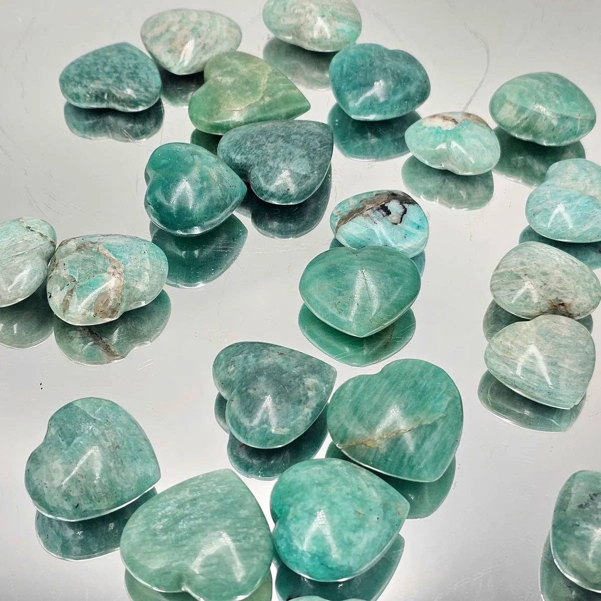 Amazonite Crystal Pocket Hearts scattered on a reflective surface, showcasing their soothing turquoise tones.