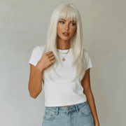 Woman with long blonde hair wearing a white t-shirt and blue jeans against a plain background