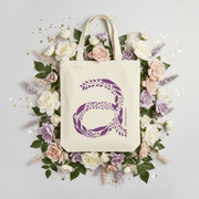 Tote bag with a purple floral design surrounded by flowers on a light gray background