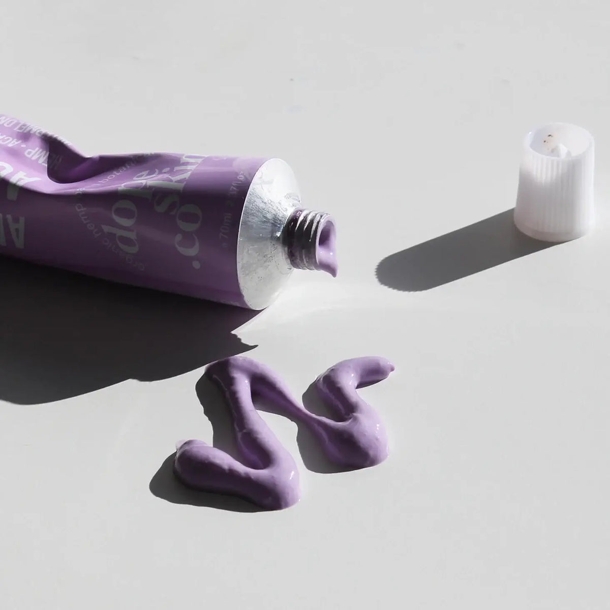 Purple tube of lip balm with a swatch on a light gray background