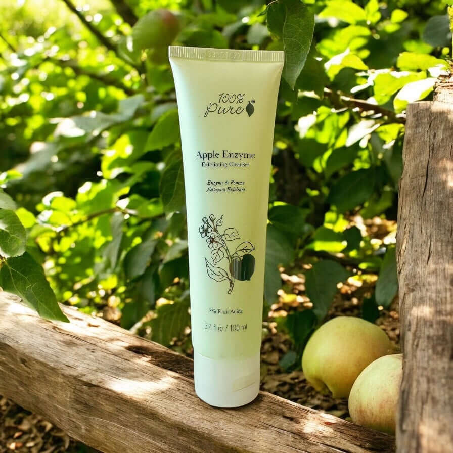 Apple Enzyme Exfoliating Cleanser from 100% Pure surrounded by greenery and apples, showcasing its natural exfoliating properties.