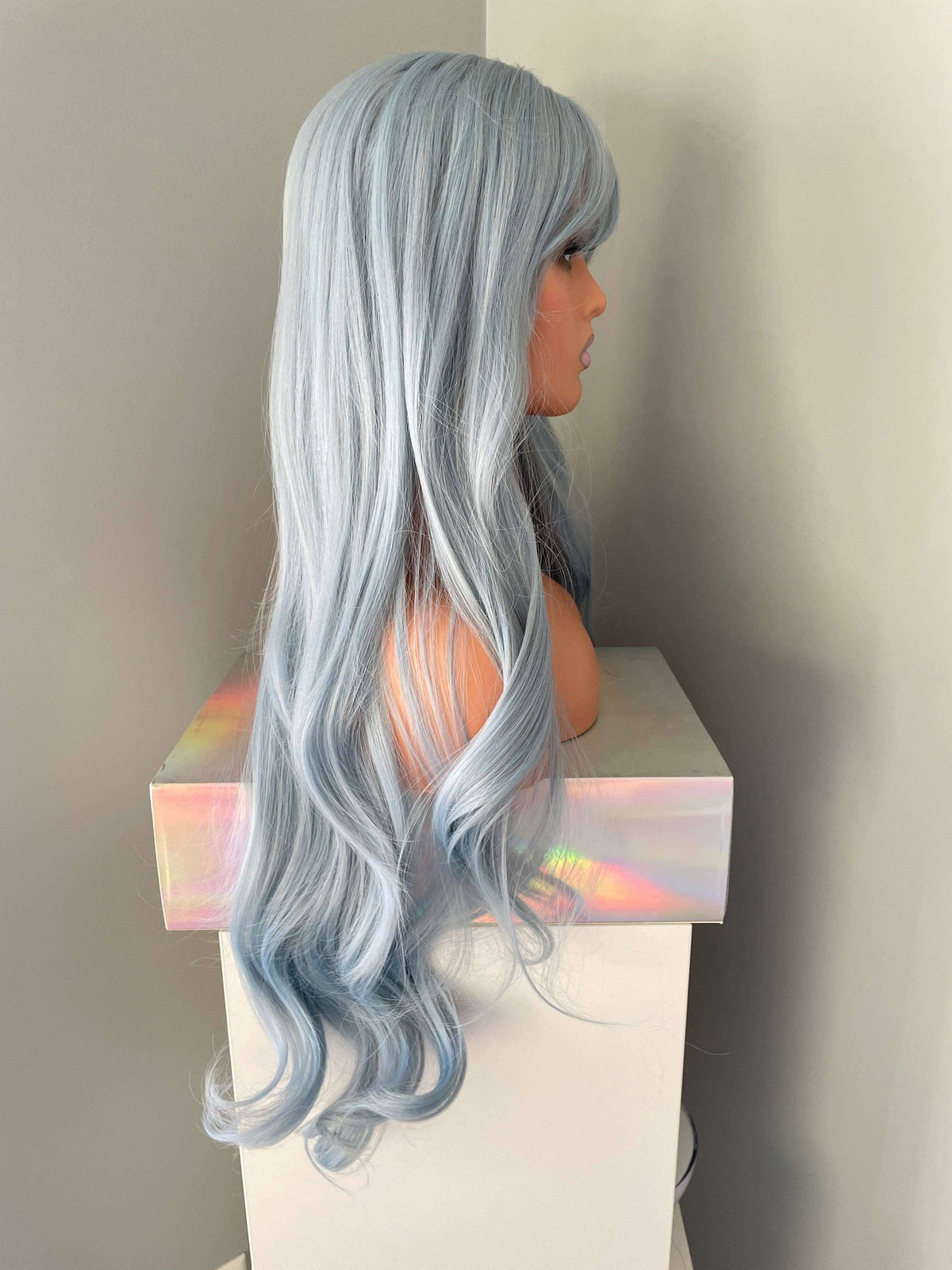 Azura Long Light Pastel Blue Wig displayed side view on stand, showcasing soft waves in a dreamy blue shade.