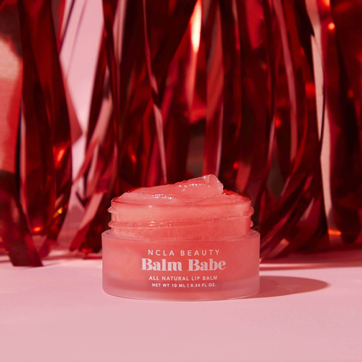 NCLA Beauty Balm Babe lip balm jar with a red textured background
