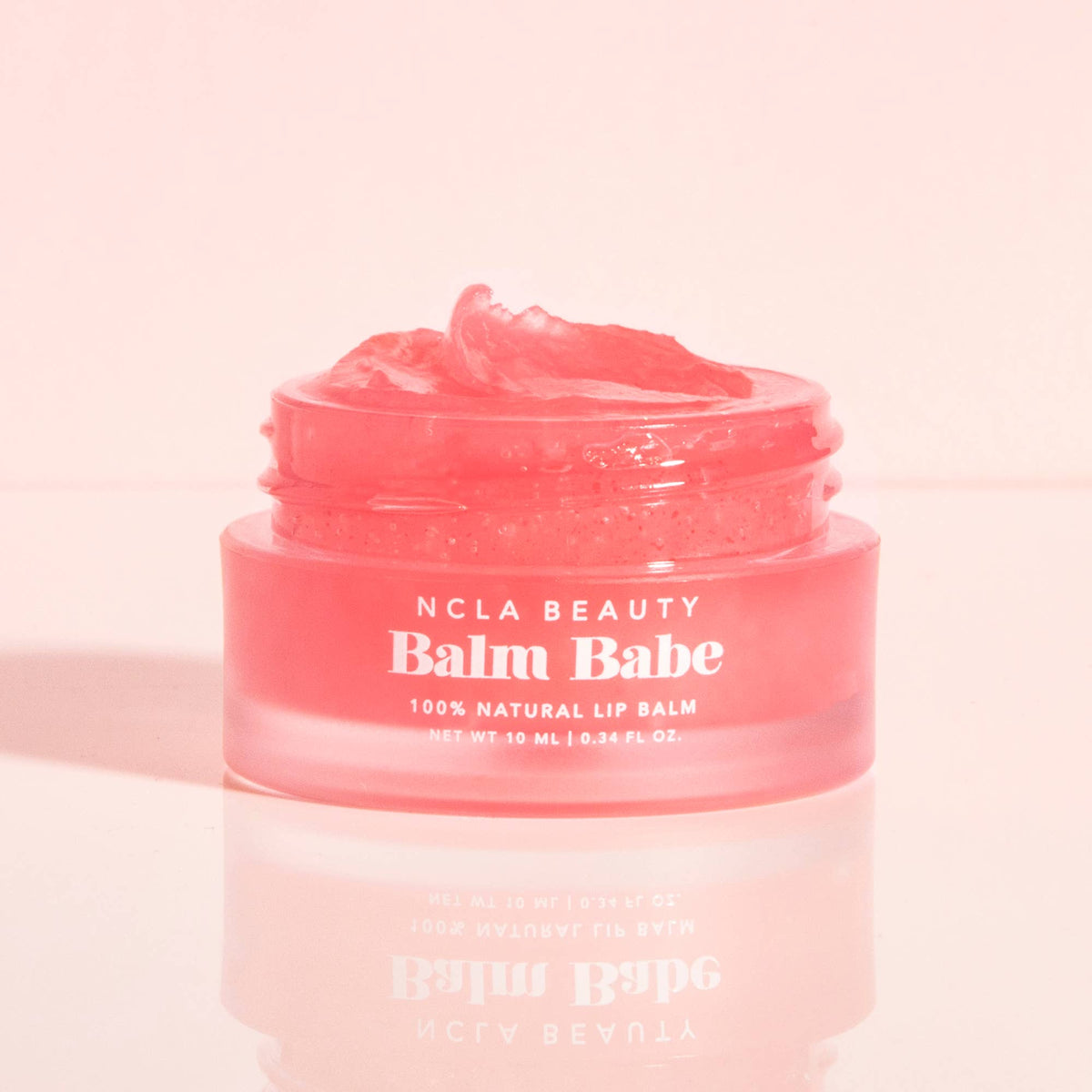 Pink lip balm jar labeled 'Balm Babe' by NCLA Beauty on a pink background