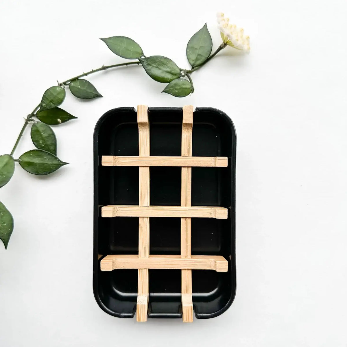 Black rectangular tray with wooden grid on a white background with green leaves.