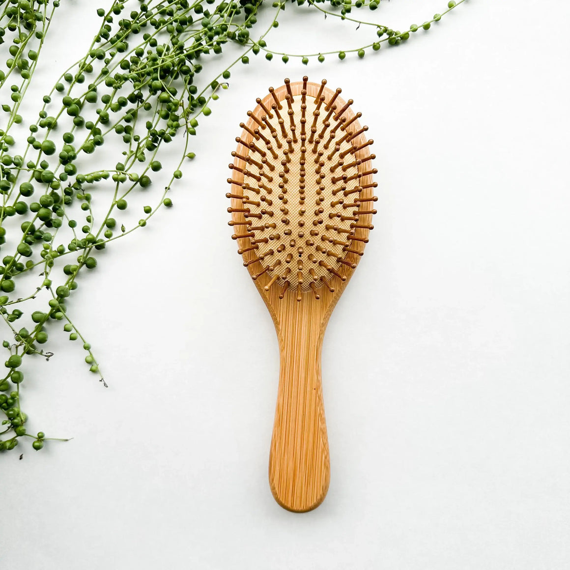 Bamboo Hair Brush on a white surface surrounded by greenery, designed to reduce static and frizz.