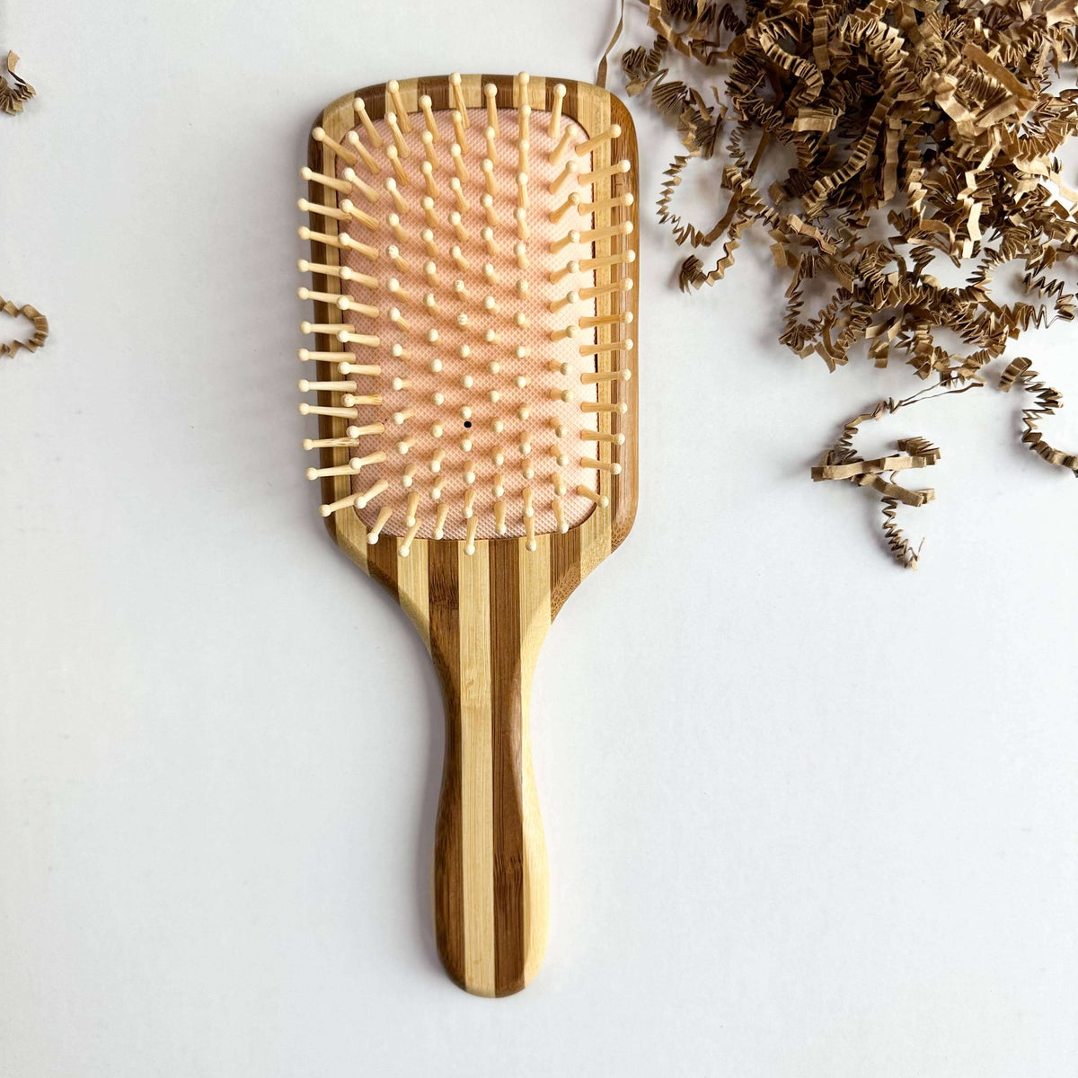 Bamboo Hair Brush - Smile Boutiques on a white background with curly paper shreds.