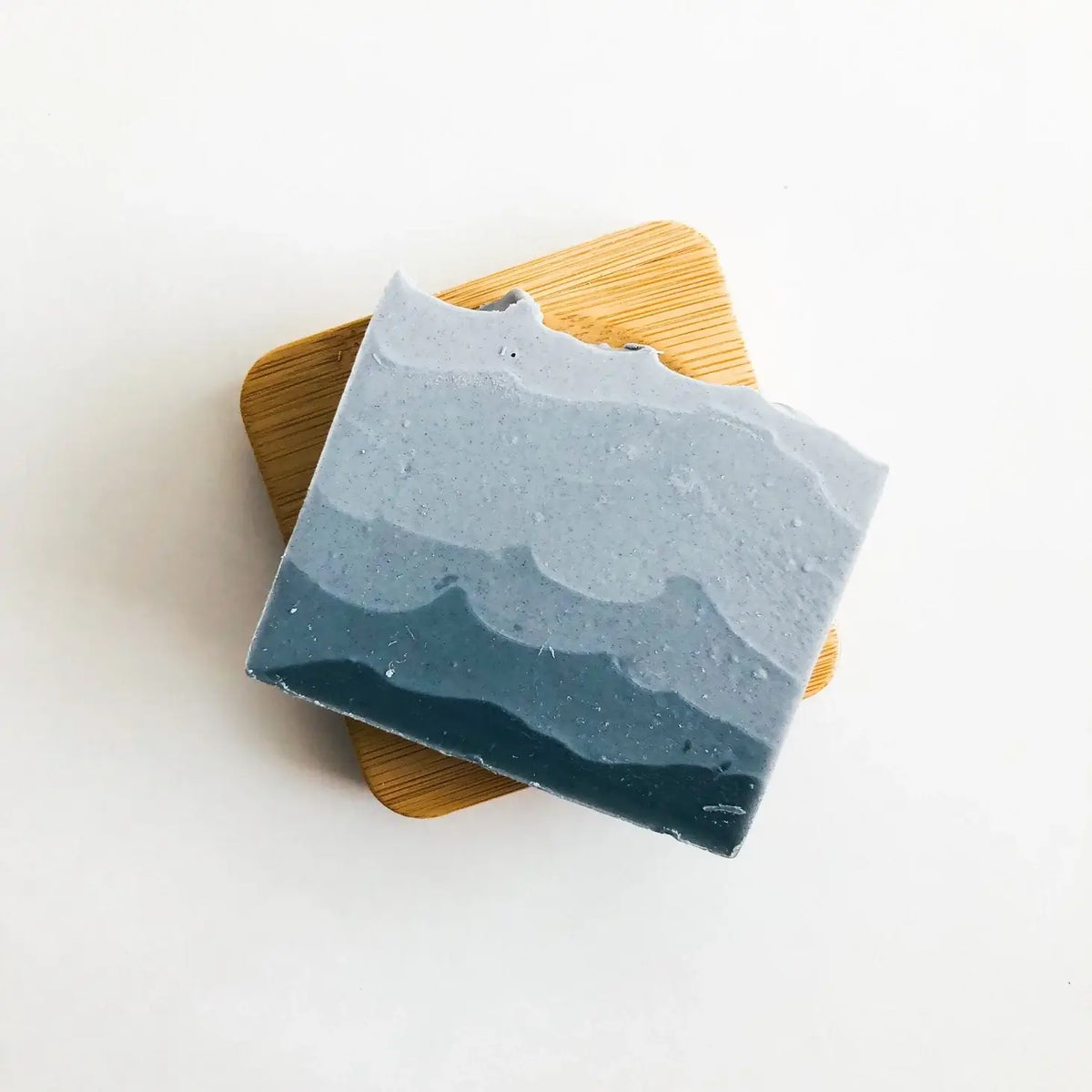 Blue and gray layered soap on a wooden coaster with a white background