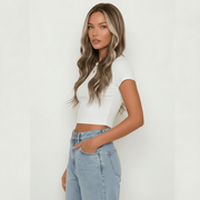 Woman wearing a white crop top and light blue jeans against a plain background