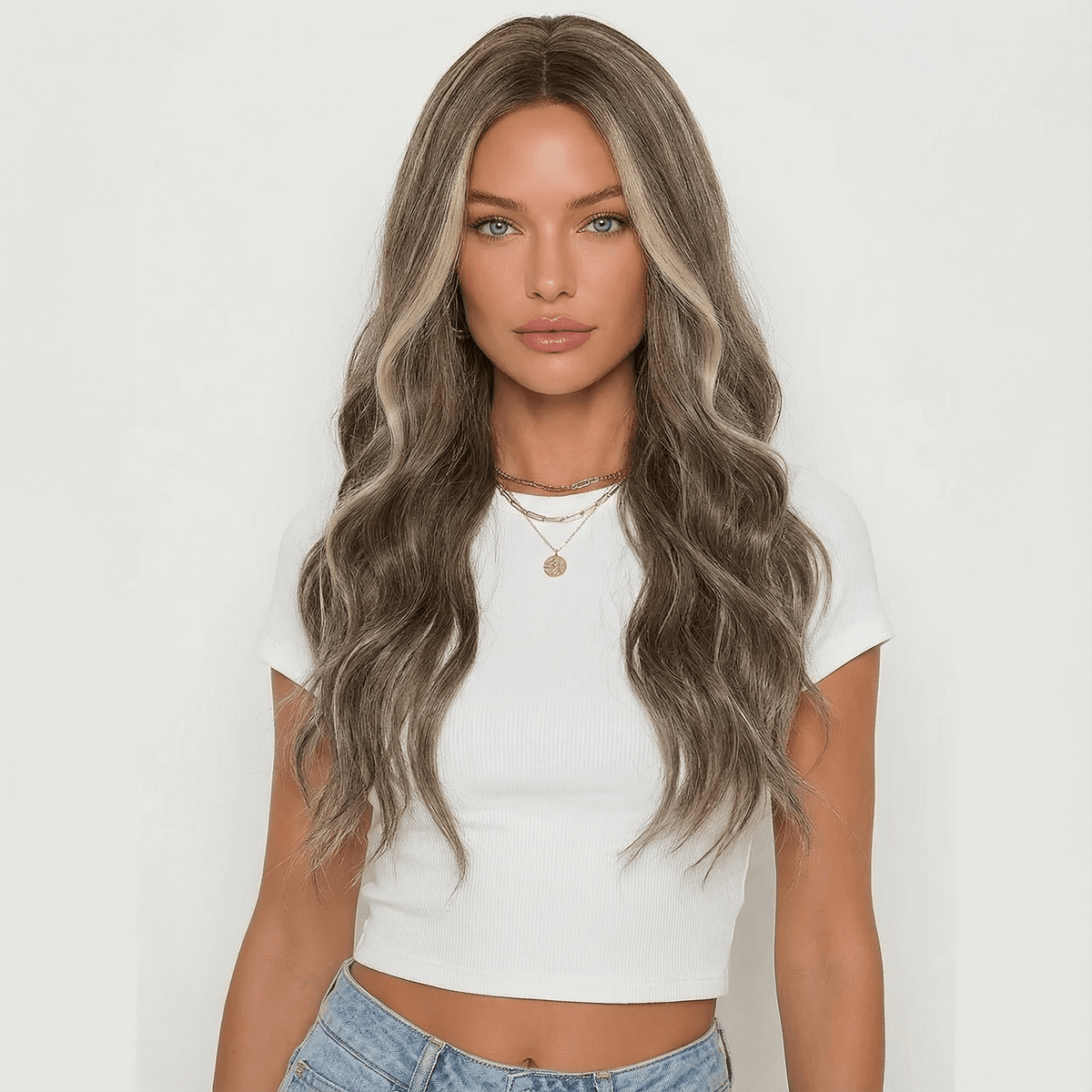 Woman with long wavy hair wearing a white crop top and blue jeans on a plain background