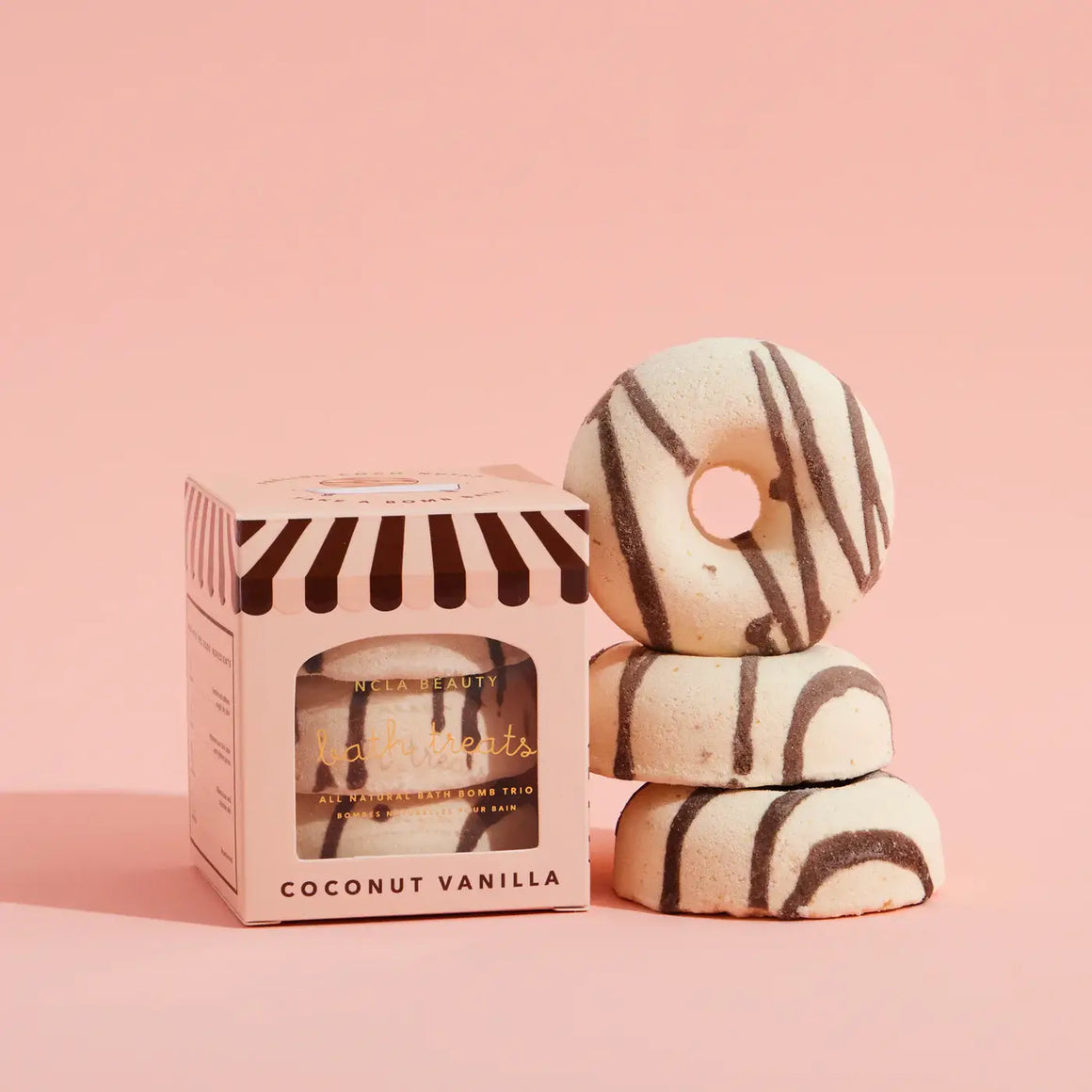 Stack of coconut vanilla bath bombs with a striped box on a pink background