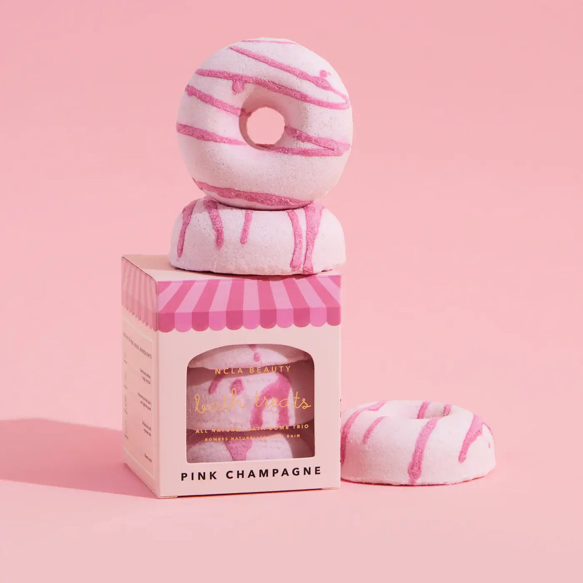 Pink and white striped donut-shaped bath bombs in a striped box on a pink background