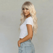 Blaire Ash Blonde Beach Wave Synthetic Wig with Bangs styled on a model in a white crop top and jeans.
