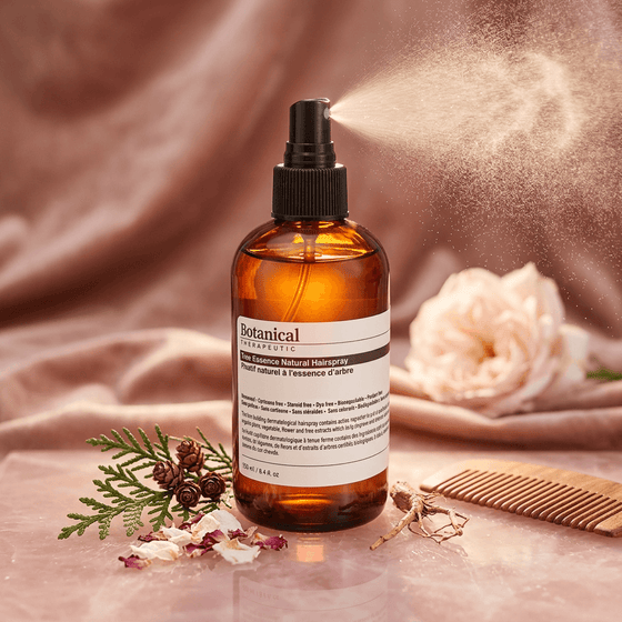 Botanical Therapeutics hairspray  bottle with a label on a pink fabric background with flowers and a comb.