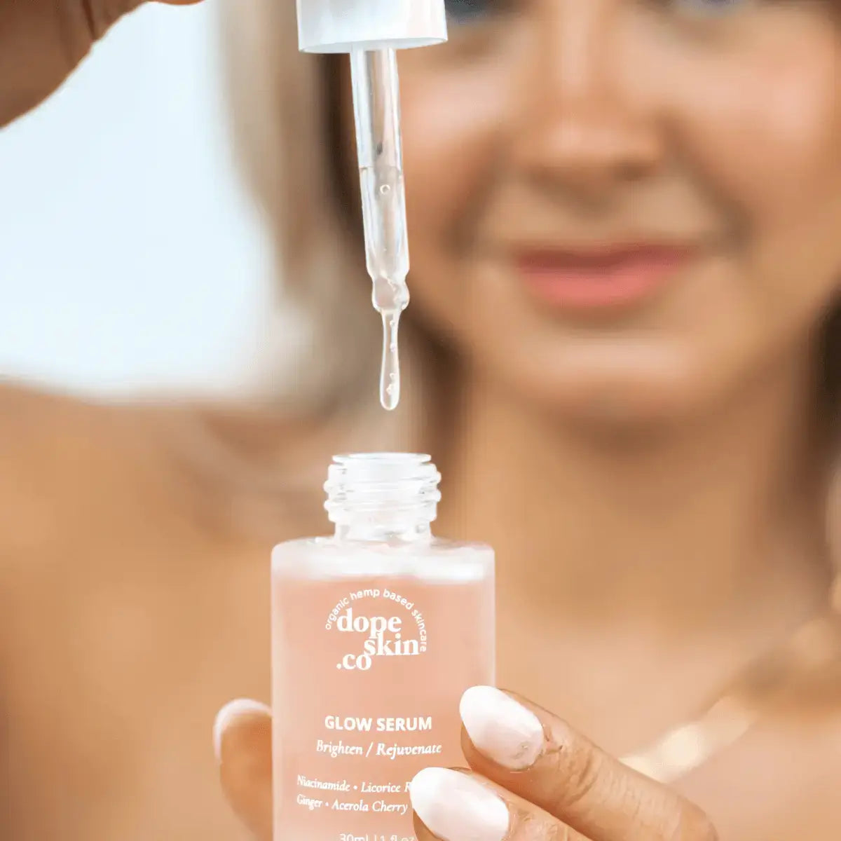 Person holding a 'dope skin co.' glow serum with a dropper above it.