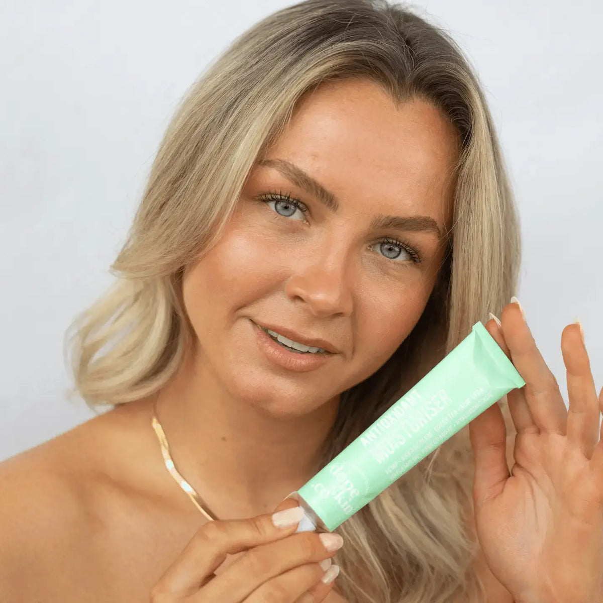 Woman holding a green tube of cream against a plain background