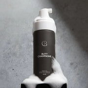 Bottle of 'Butt Champagne' with a foamy texture against a gray background
