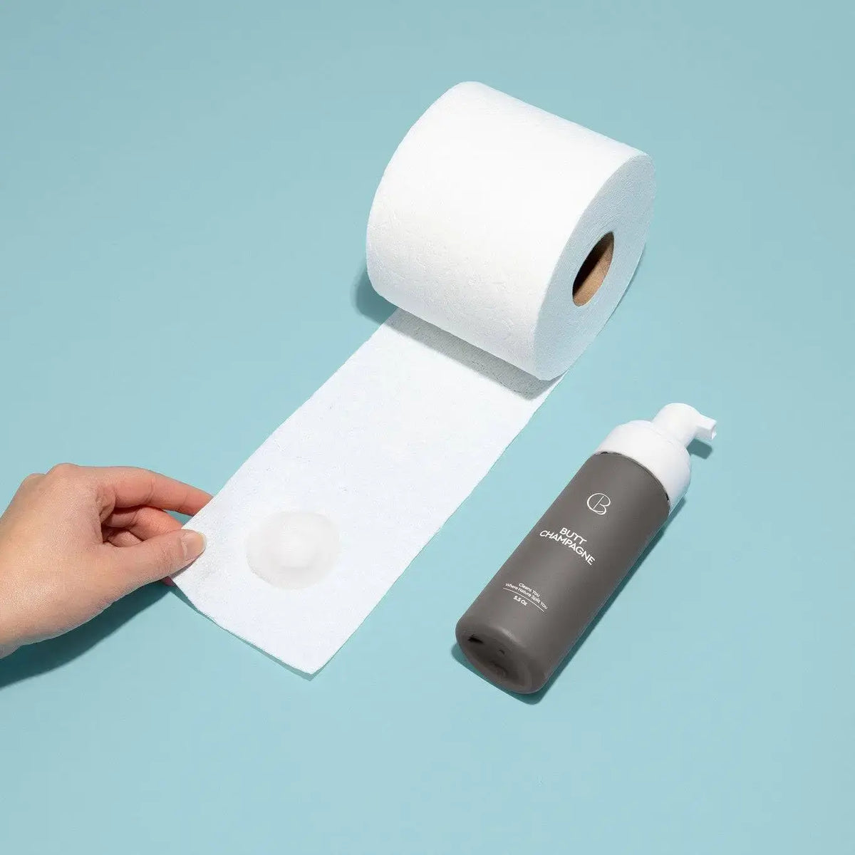 Roll of toilet paper with a hand holding it, next to a bottle of cleaning solution on a light blue background
