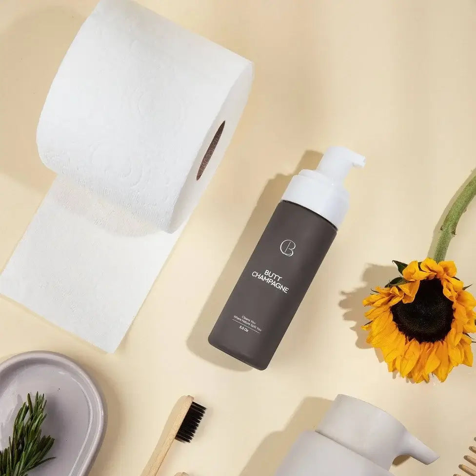 Collection of eco-friendly products including a black bottle, white dispenser, bamboo toothbrush, and sunflowers on a beige background.