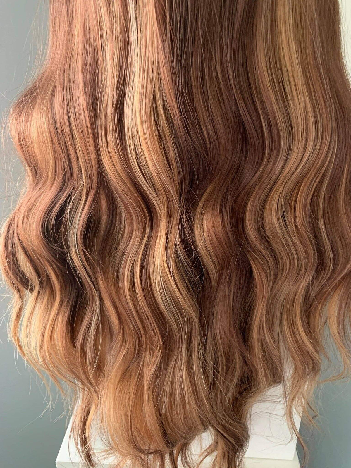 Close-up of wavy hair with brown and blonde tones on a neutral background