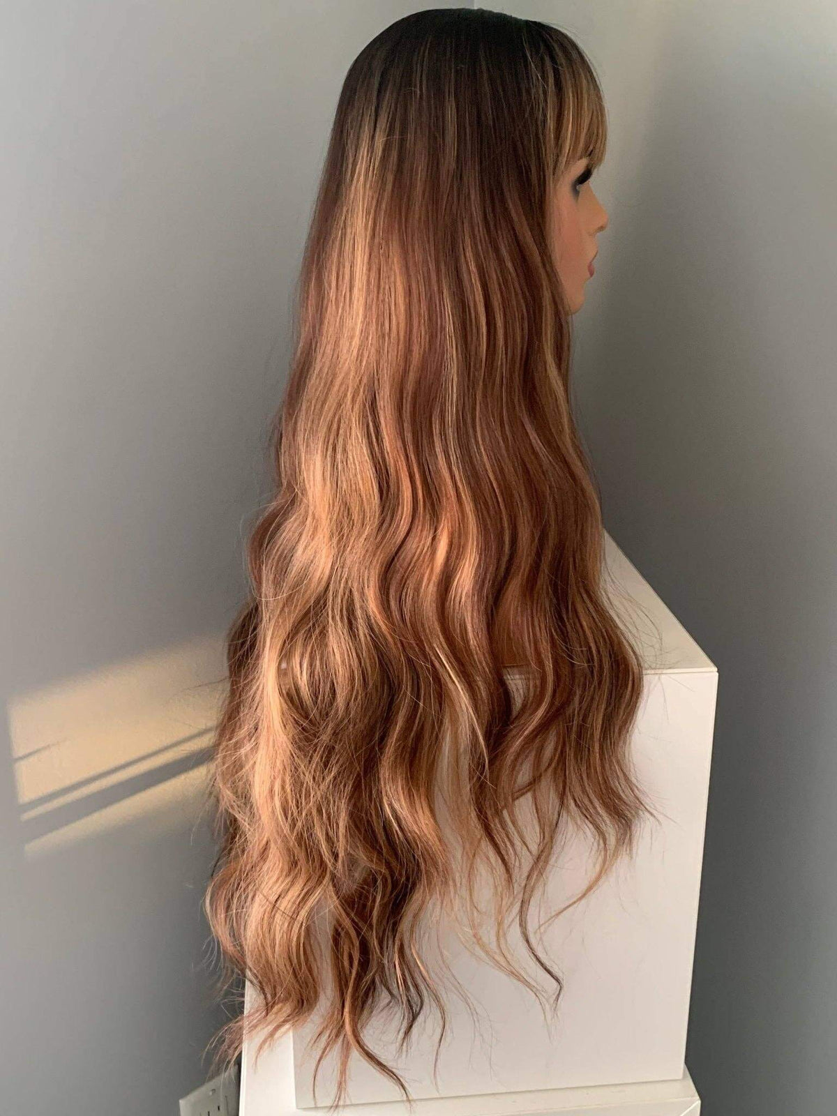 Long, wavy brown hair on a mannequin head against a neutral background