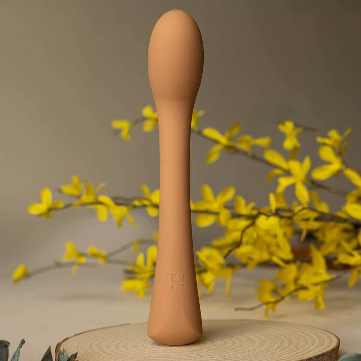 Cecily Curved G-Spot and Wand-Style Vibrator, a sleek curved g-spot vibrator on a wooden base with yellow flowers.
