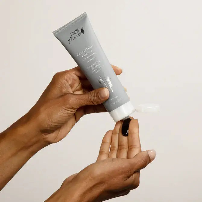 Hands holding 100% Pure Charcoal Clay Cleanser tube, dispensing product for a refreshing facial cleanse.