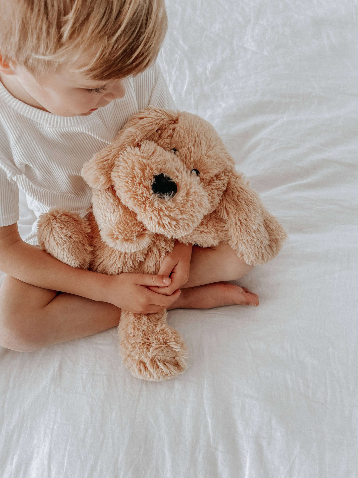 Child cuddling Charlie The Weighted Puppy Dog Teddy plush toy on a bed, promoting comfort and emotional wellbeing.