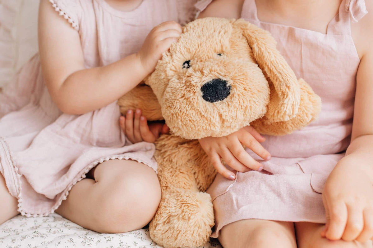 Two children hugging Charlie The Weighted Puppy Dog Teddy on a cozy bed.