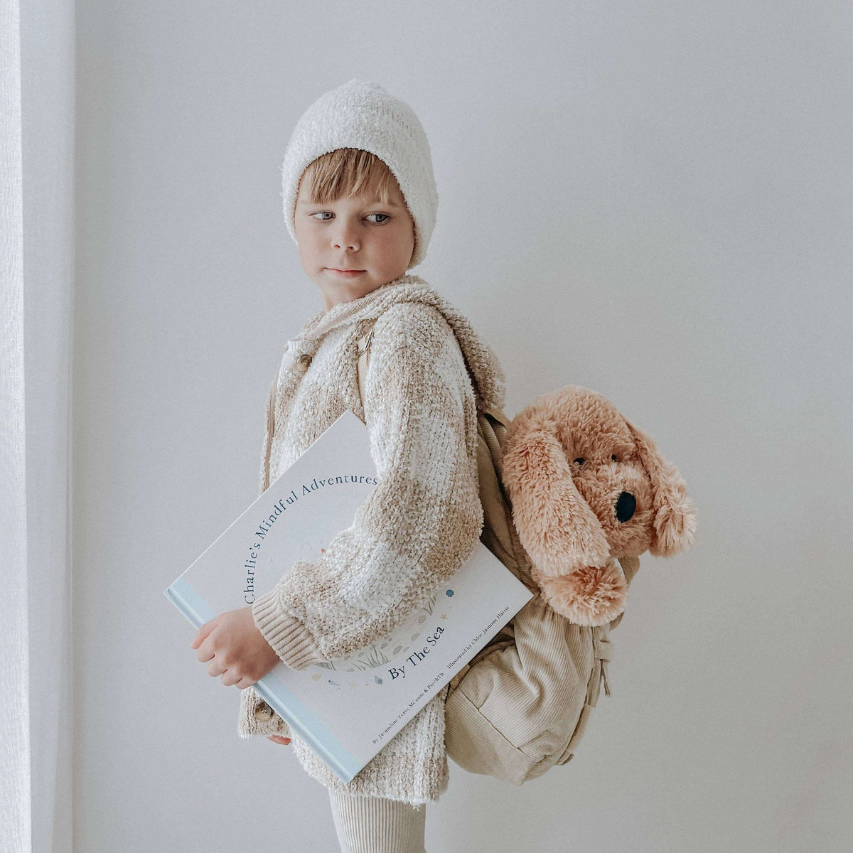Child holding a book and carrying Charlie The Weighted Puppy Dog Teddy in a backpack.