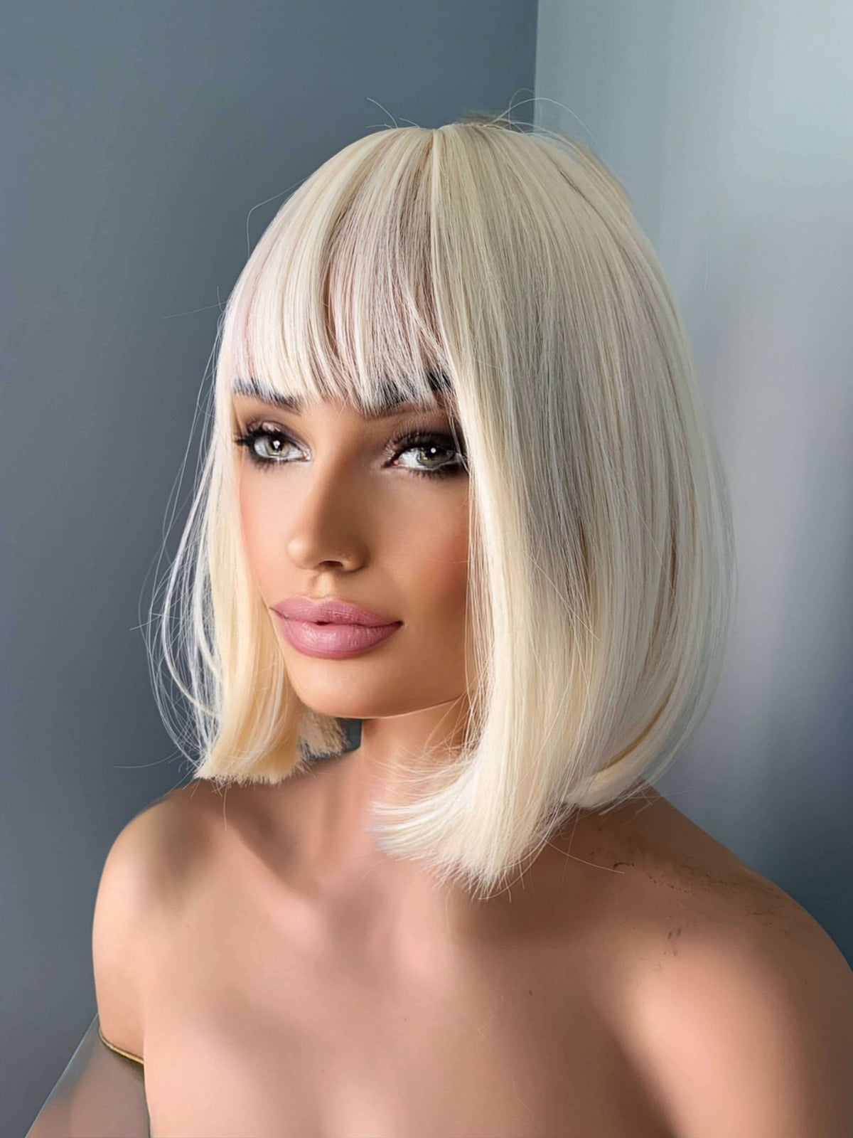 Woman with a stylish blonde bob wig against a plain background