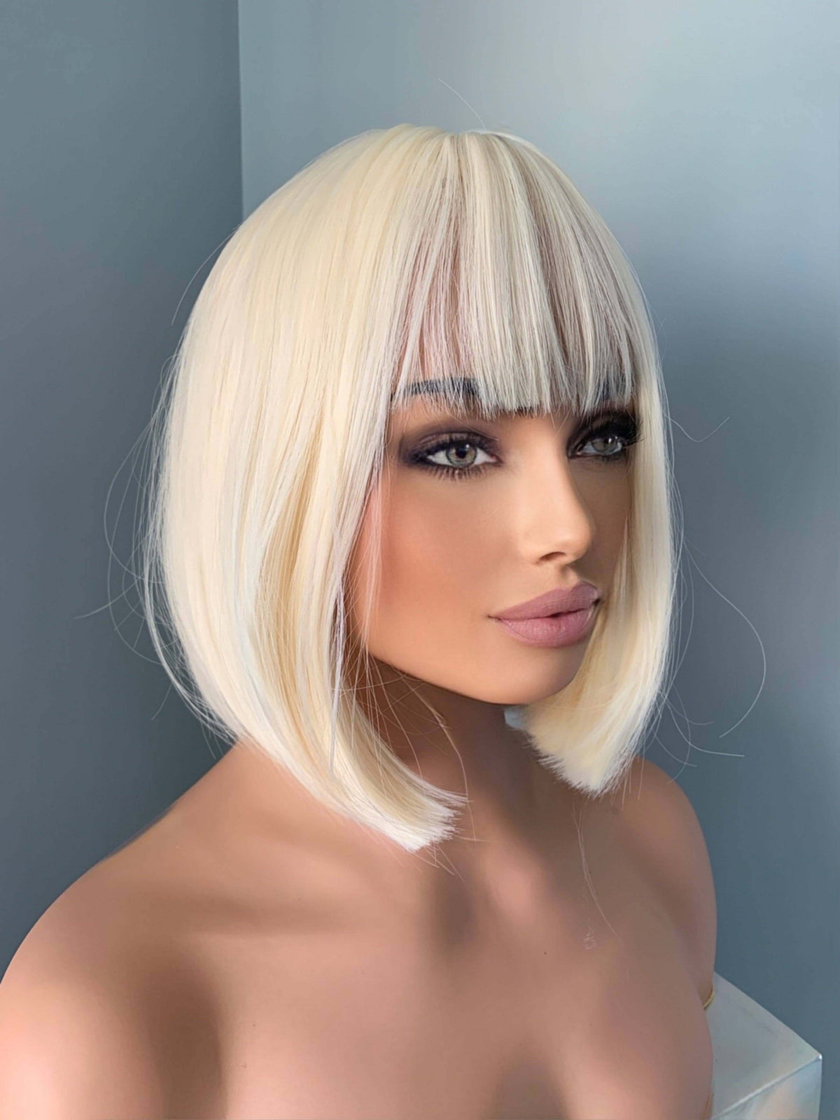 Woman wearing a blonde wig with bangs against a gray background