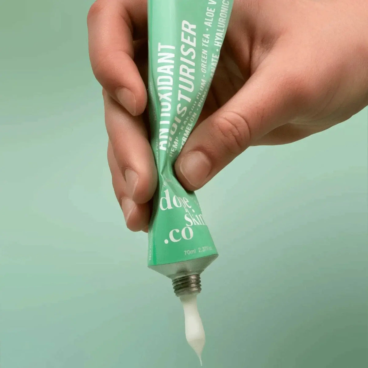 Hand holding a green tube of moisturizer with visible brand name against a light green background
