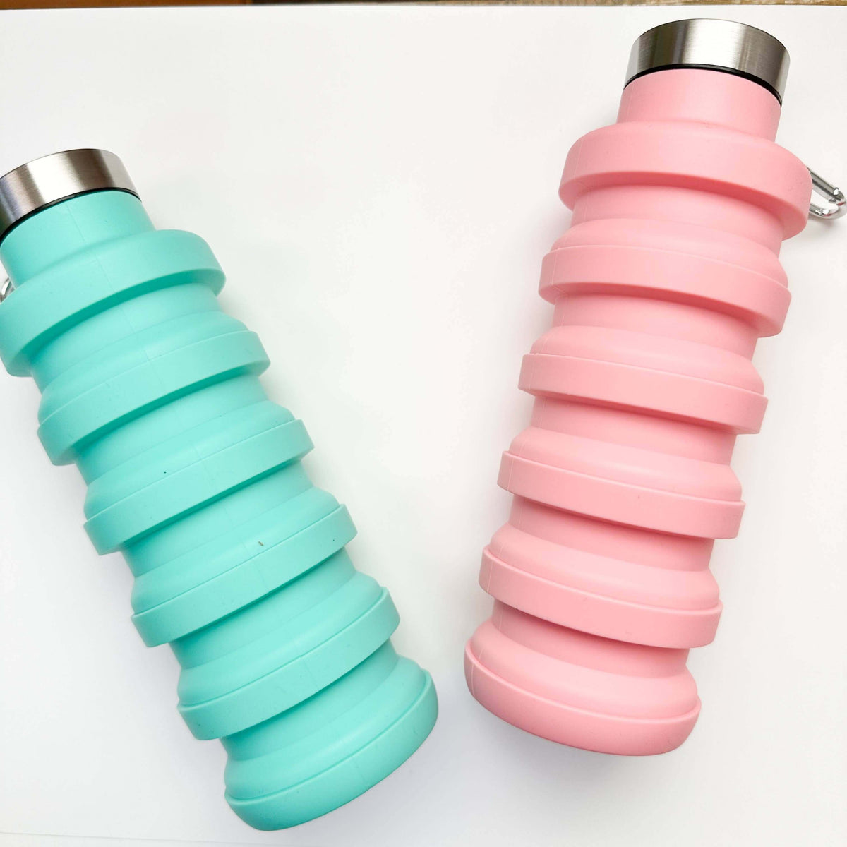 Two collapsible water bottles, one teal and one pink, on a white background.