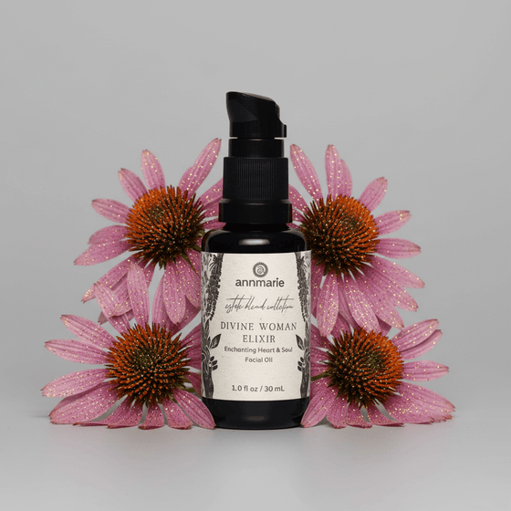 Black bottle labeled 'Divine Woman Elixir' surrounded by pink flowers on a gray background